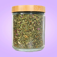 Load image into Gallery viewer, Glass jar with dried herbs and a bamboo lid on a purple background
